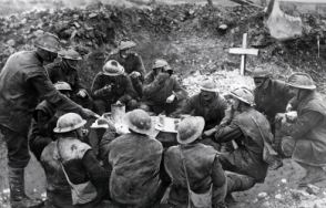 Soldiers on the Western Front in a happy mood as they eat a meal to celebrate Christmas Day in a shell hole partly occupied by the grave of a comrade.